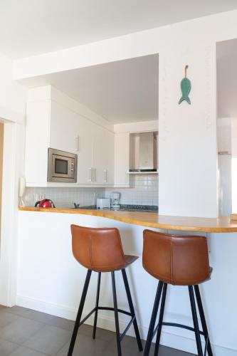 a kitchen with white cabinets and two bar stools at Vistas al Mar junto a la playa 3B in Poris de Abona