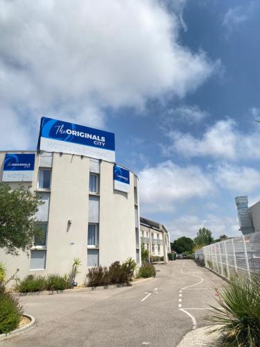 a building with a blue sign on the side of it at The Originals City, Hôtel Les Dômes, Perpignan Sud Saleilles in Perpignan