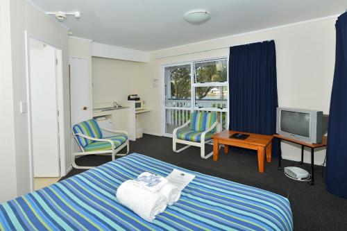 a bedroom with a bed and two chairs and a television at Acacia Lodge Motel in Mangonui