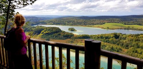 a woman standing on a balcony overlooking a lake at Le Jura en toutes saisons Piscine, SPA, location VTT, balades 2cv, climatisation in Bonlieu