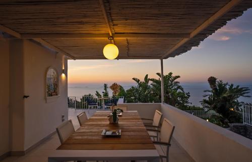d'une table et de chaises en bois sur un balcon avec vue sur le coucher du soleil. dans l'établissement Capri Blue Luxury Villa Le Tre Monelle, à Anacapri