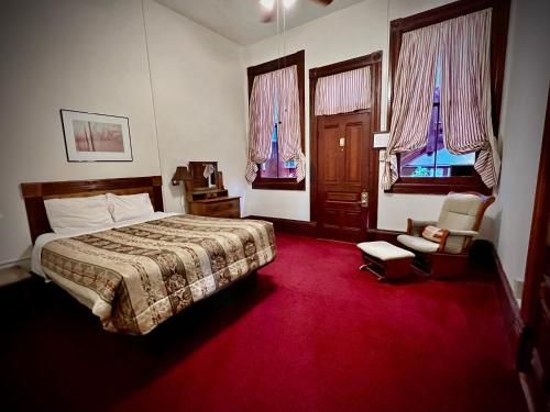 a bedroom with a bed and a chair and windows at The Monarch Hotel in Port Townsend