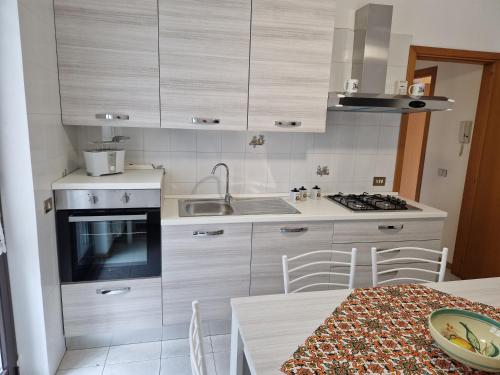 kuchnia z białymi szafkami, stołem i zlewem w obiekcie L'Isola e i Faraglioni house w mieście Aci Trezza