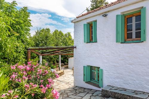 a white house with green windows and flowers at La Belle Merle in Panormos Skopelos