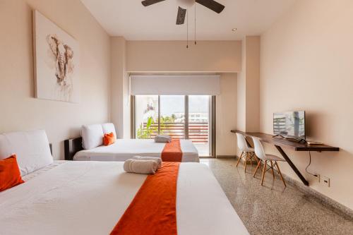 two beds in a room with a desk and a window at Infinito Condos in Playa del Carmen
