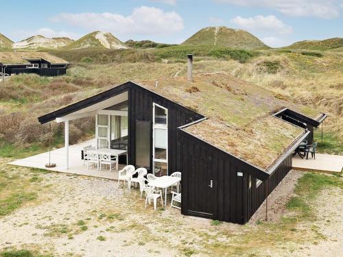 a black house with a grass roof with a table and chairs at 8 person holiday home in Pandrup in Blokhus