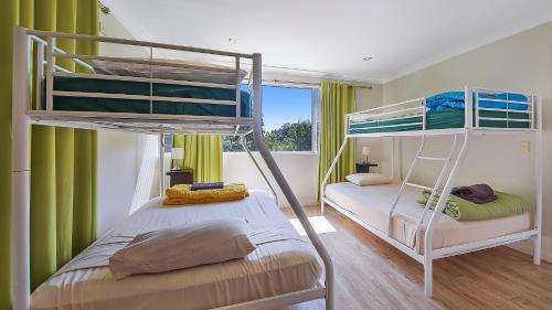 two bunk beds in a room with green curtains at Ohana Beach House in Tangalooma
