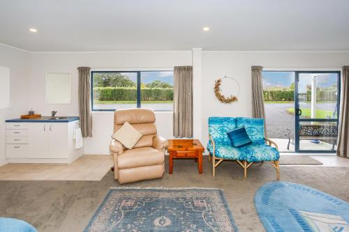 a living room with a chair and a table and windows at Self Contained Cottage Pukekohe in Auckland