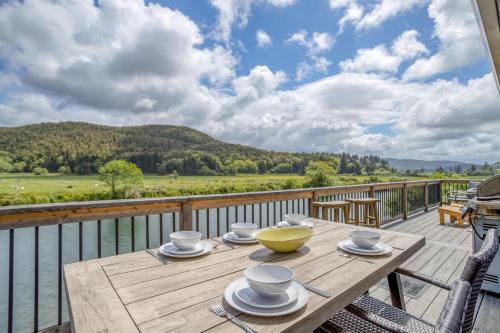a wooden table on a deck with a view of the water at Riverfront Gem - Meredith Lodging in Cloverdale