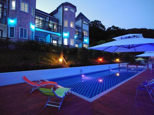 a house with a swimming pool and two chairs and an umbrella at Beljari Pension in Tongyeong