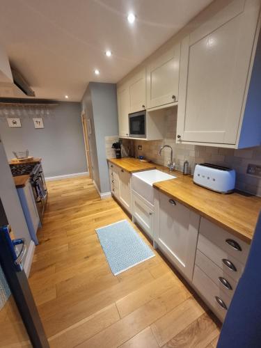 a kitchen with white cabinets and a wooden floor at Neet Retreat - sleeps 7 next to beach in Bude