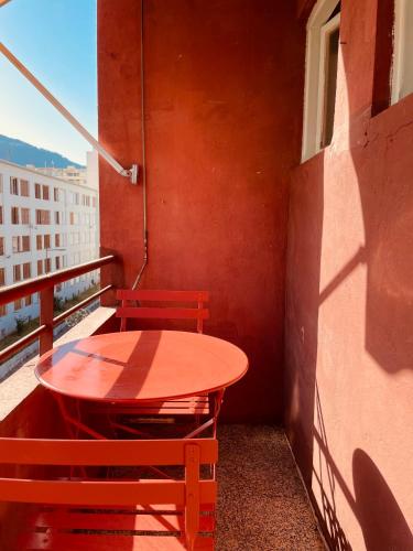 une table rouge et un banc assis sur un balcon dans l'établissement Appartement Bonaparte centre ville d'Ajaccio, à Ajaccio