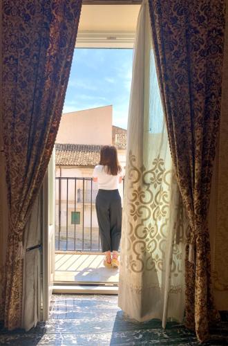 a woman standing on a balcony looking out the window at Scicli Albergo Diffuso in Scicli