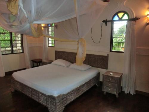 a bedroom with a bed with a canopy and two windows at Villa Lamuhouse Diani Beach in Diani Beach