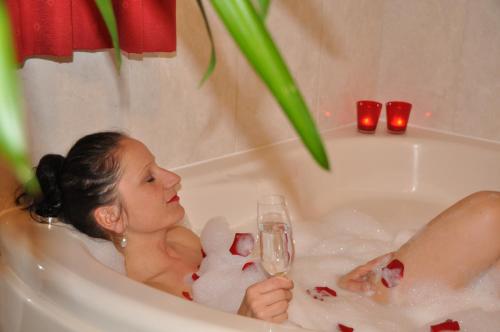 a woman sitting in a bath tub with a glass of champagne at Appartementhaus Grill in Strobl