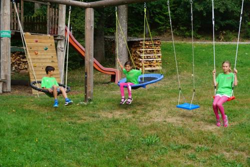 three children sitting on swings in a playground at Gasthof Pension Fischerstüberl in Blaibach