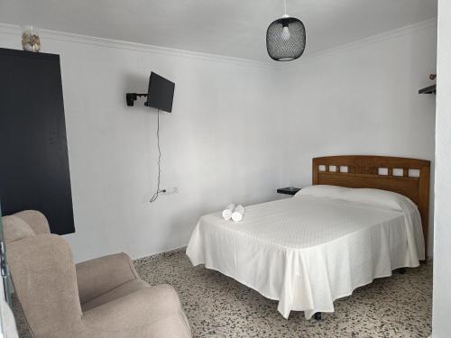 a white bedroom with a bed and a chair at Alojamientos La Menúa in Los Badalejos