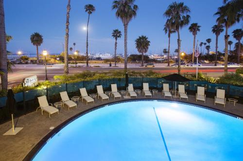een zwembad met stoelen en palmbomen in de nacht bij West Beach Inn, a Coast Hotel in Santa Barbara