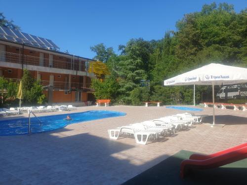 een zwembad met witte tafels en stoelen en een parasol bij Hotel Maria in Kiten