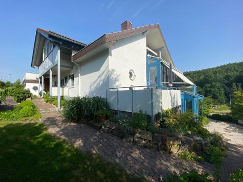 a white house with blue trim on a hill at Pension Liesbachtal direkt am Waldrand Bayerische Rhön in Schönau an der Brend