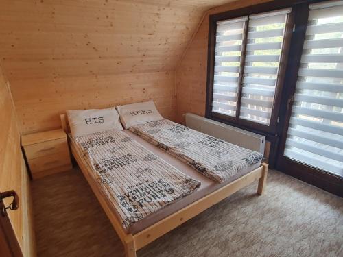 uma cama num quarto de madeira com 2 janelas em Cabana DEMI em Gheorgheni