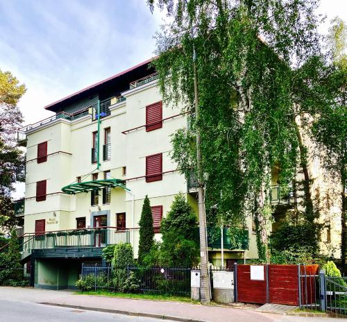 a white building with red windows and a tree at Apartament Jurata 30 in Jurata