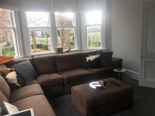a brown couch in a living room with windows at Aratahi Cottages - West Wing in Carterton