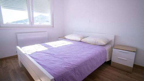 a bedroom with a bed with purple sheets and a window at Casa llena in Seget Vranjica