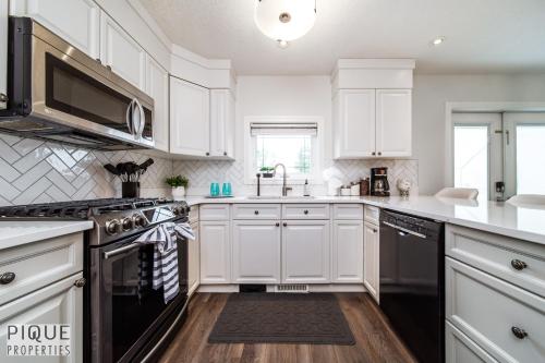 a kitchen with white cabinets and a sink and a stove at LUXURIOUS 6 Bed Home I Fireplace I near Sports Park I with Double Garage & Fast WiFi! in Edmonton