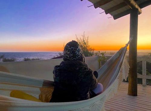 a person sitting in a hammock watching the sunset at Bella Vista Kitnets in Farol de Santa Marta