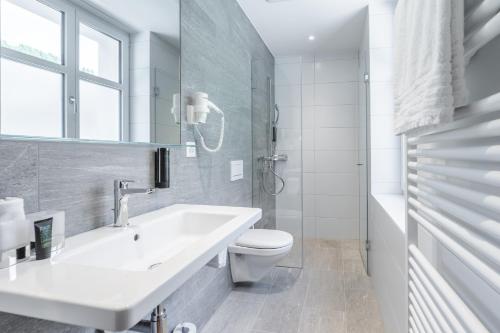 a white bathroom with a sink and a toilet at Hotel Alpensonne - Panoramazimmer & Restaurant in Arosa