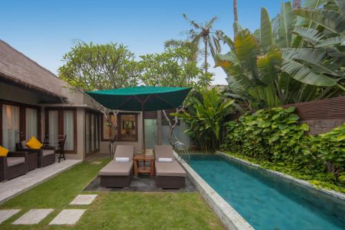 a pool with a table and chairs next to a house at Legian Beach Hotel in Legian