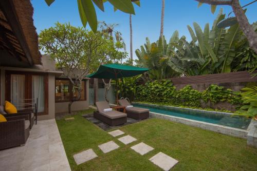 a backyard with a pool with chairs and an umbrella at Legian Beach Hotel in Legian