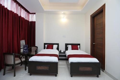 two beds in a room with a desk and red curtains at Super Hotel O Royal Inn in Faridabad