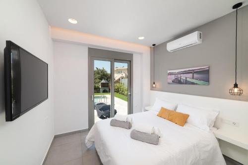 a white bedroom with a large bed and a tv at Villa Ampela by PosarelliVillas in Agia Marina Nea Kydonias