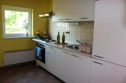 cocina con armarios blancos, fregadero y ventana en Počitniška hiška pod Hadikom, en Lendava