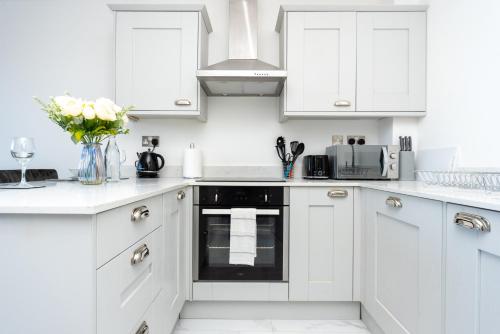 a white kitchen with white cabinets and flowers in a vase at Beautiful Apartments in Kings Lynn Town Centre in King's Lynn
