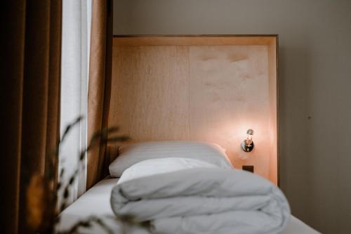 a bed with white sheets and a light on a wall at Hotel Müllers Self-Check-In in Arbon