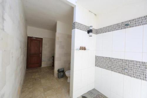 a bathroom with a toilet and a tiled wall at Aaliku Bungalows in Gili Trawangan