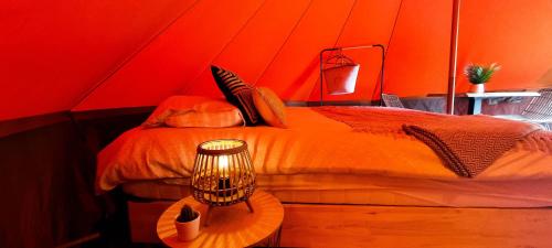Fiertelmeers Boutique Glamping في رونس: غرفة حمراء بها سرير وطاولة بها مصباح