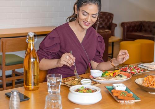 a woman sitting at a table eating food at Bloom Hotel - Brookefield in Bengaluru