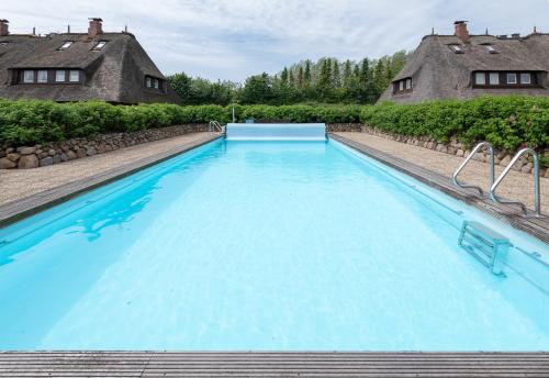 a large swimming pool with blue water in front of two houses at Bens Hüs in Braderup