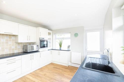 uma cozinha com armários brancos e um balcão preto em Elmsway - Southbourne em Southbourne
