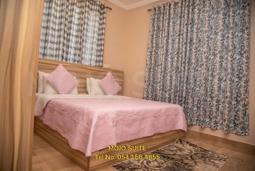 a bedroom with a bed with pink sheets and a window at Mojo Apartment, Tema in Tema