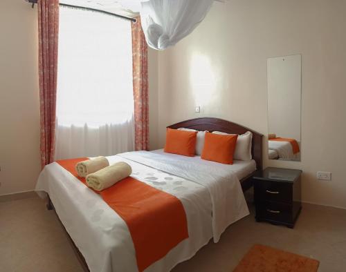 ein Schlafzimmer mit einem Bett mit orangefarbenen Kissen und einem Fenster in der Unterkunft MILIMANI DRIVE LIVINGs in Kisumu