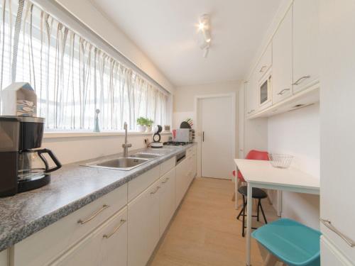 a kitchen with white cabinets and a sink and a table at Holiday Home Klemskerkestraat by Interhome in Bredene