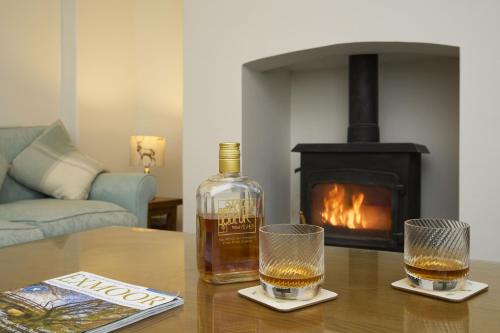 a bottle of whiskey and two glasses on a table with a fireplace at 1 Lower Spire in Dulverton