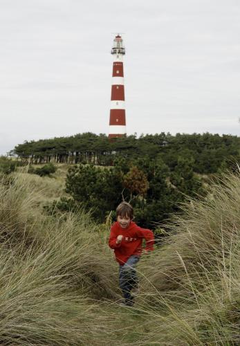 a young boy walking through the grass in front of a lighthouse at Sier aan Zee in Hollum