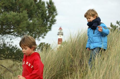 two children standing in tall grass with a lighthouse in the background at Sier aan Zee in Hollum