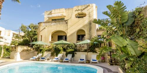 um resort com uma piscina e cadeiras e um edifício em Villa Xemxija em Xlendi